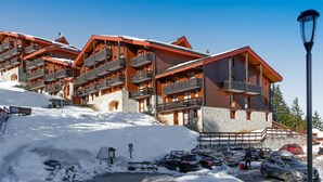 A multi-story hotel with balconies, a parking area, and a clear blue sky. - Cozy Retreat in Courchevel: 4 People, Ski-in/Ski-out, Wifi (Courchevel 1550)