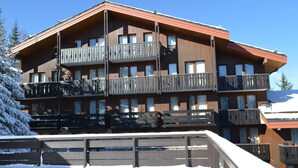 A multi-story wooden building with balconies, likely a hotel or lodge. - Cozy Retreat in Courchevel: 4 People, Ski-in/Ski-out, Wifi (Courchevel 1550)