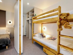 Ein Schlafraum mit Etagenbett, einem Teddybären im oberen Bett, einem kleinen Nachttisch und einer Tür zu einem anderen Raum.