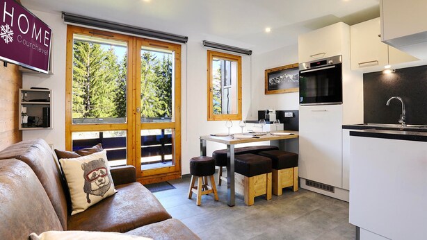 A modern kitchen with a dining area, wooden flooring, and large windows offering a view of trees. - Cozy Retreat in Courchevel: 4 People, Ski-in/Ski-out, Wifi (Courchevel 1550)