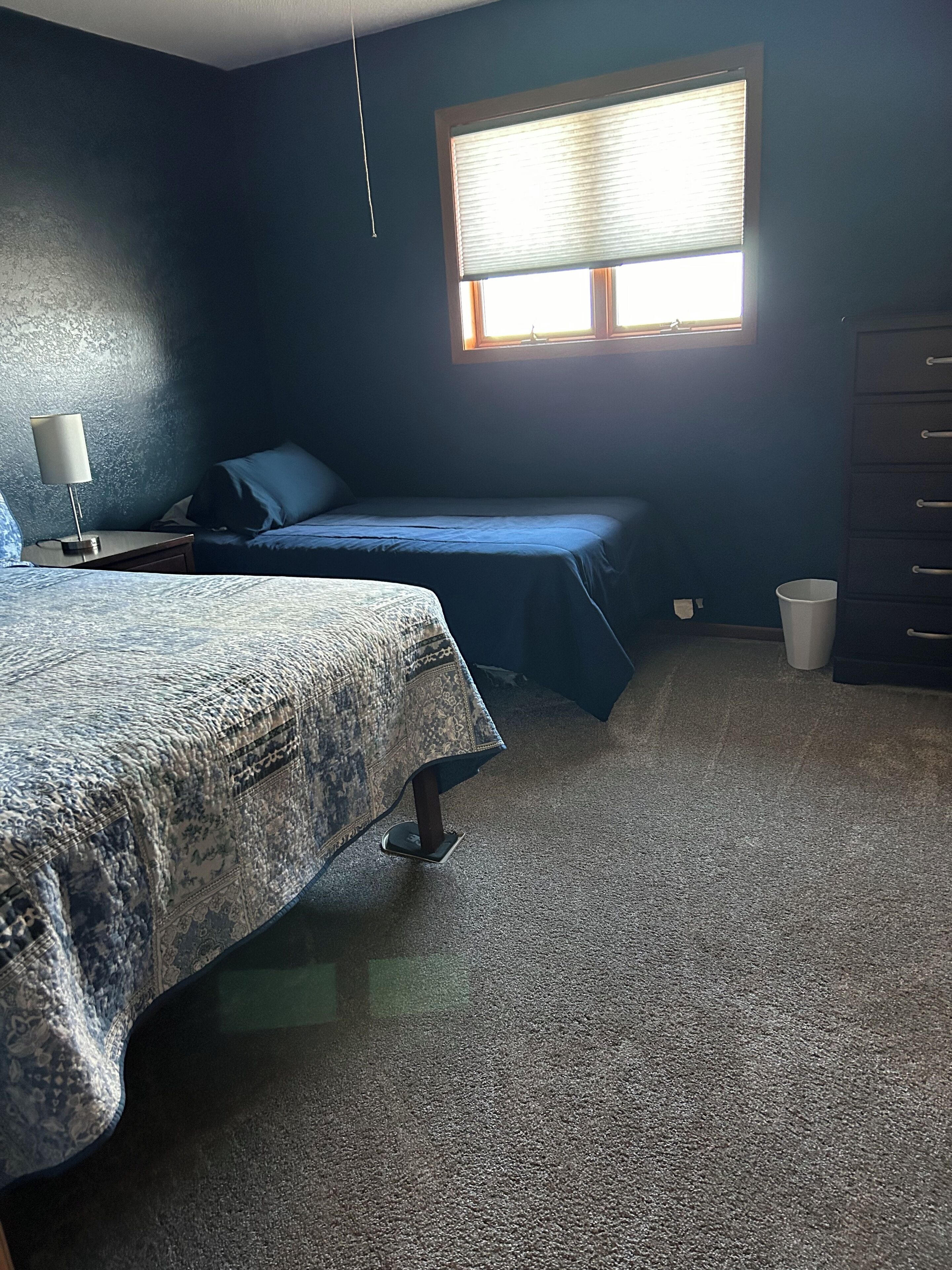 A bedroom with a bed, a nightstand, a dresser, and a window with blinds.