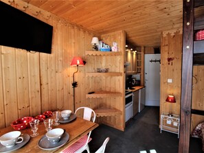 A wooden interior with a dining table set for four, a kitchen area, and a small seating area with a red lamp. - Renovated studio in Avoriaz, 4 pers, balcony, WIFI (Avoriaz)
