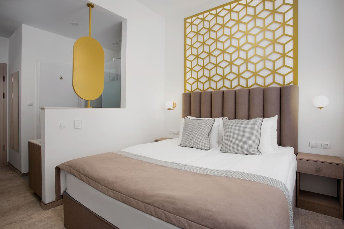 A modern hotel room with a large bed, a geometric wall panel, a bedside table, and a mirror.