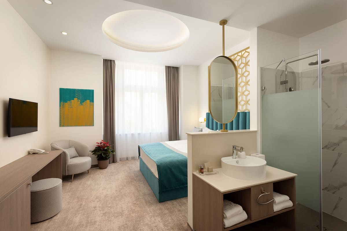 A modern hotel room with a bed, a desk, a bathroom with a shower, and a large mirror.