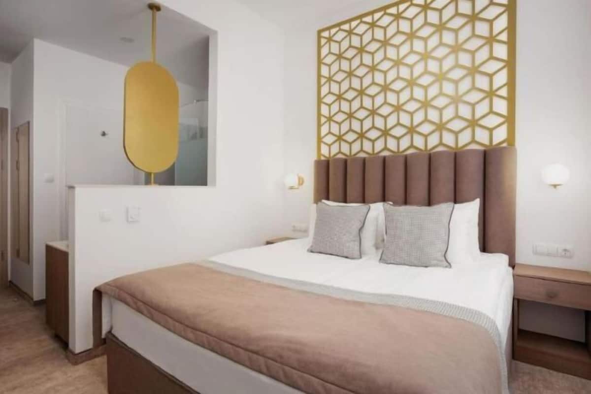 A modern hotel room with a large bed, a geometric patterned headboard, and a minimalist design.