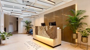 Un espace d’accueil d’hôtel doté d’un comptoir en marbre, d’un éclairage moderne et de plantes en pot.