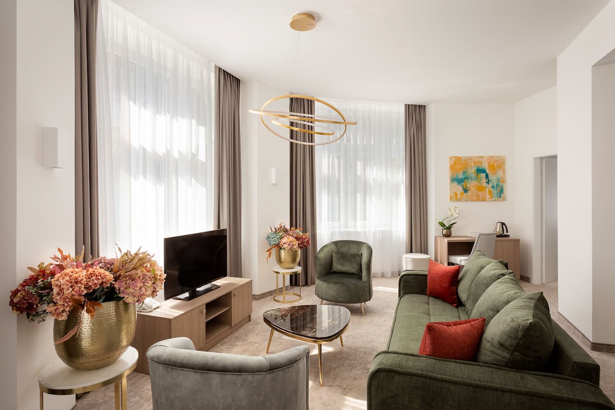 A modern living room with a green sofa, a grey armchair, a coffee table, a TV, and a decorative vase with flowers.