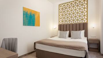 Una habitación de hotel moderna con una cama grande, un panel de pared geométrico, un cuadro de paisaje urbano y una mesita de noche pequeña con una lámpara.