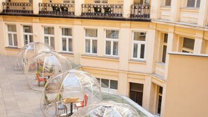 Structures en forme de dôme transparentes, dotées de sièges et de plantes en pot sur un sol carrelé, se dressent devant la façade d’un immeuble agrémenté de balcons et de fenêtres.