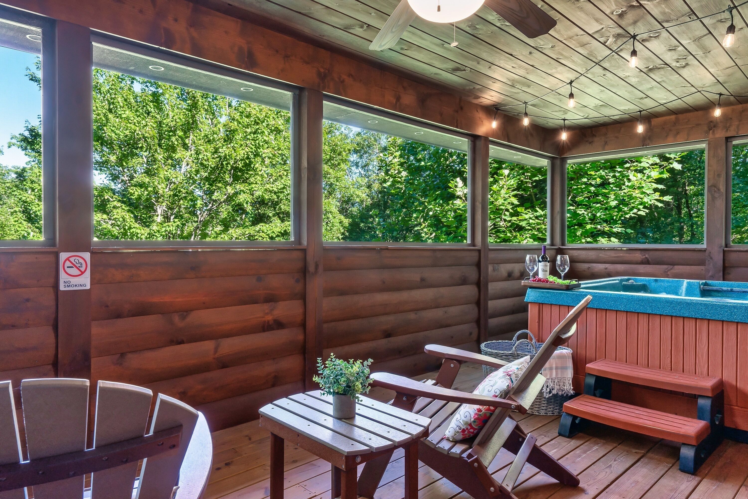 Una terraza de madera con jacuzzi, zona de estar y grandes ventanales con vistas a la vegetación.