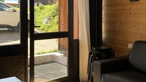 A room with a wooden wall, a window with a view of a parked car and greenery outside, and a black chair.