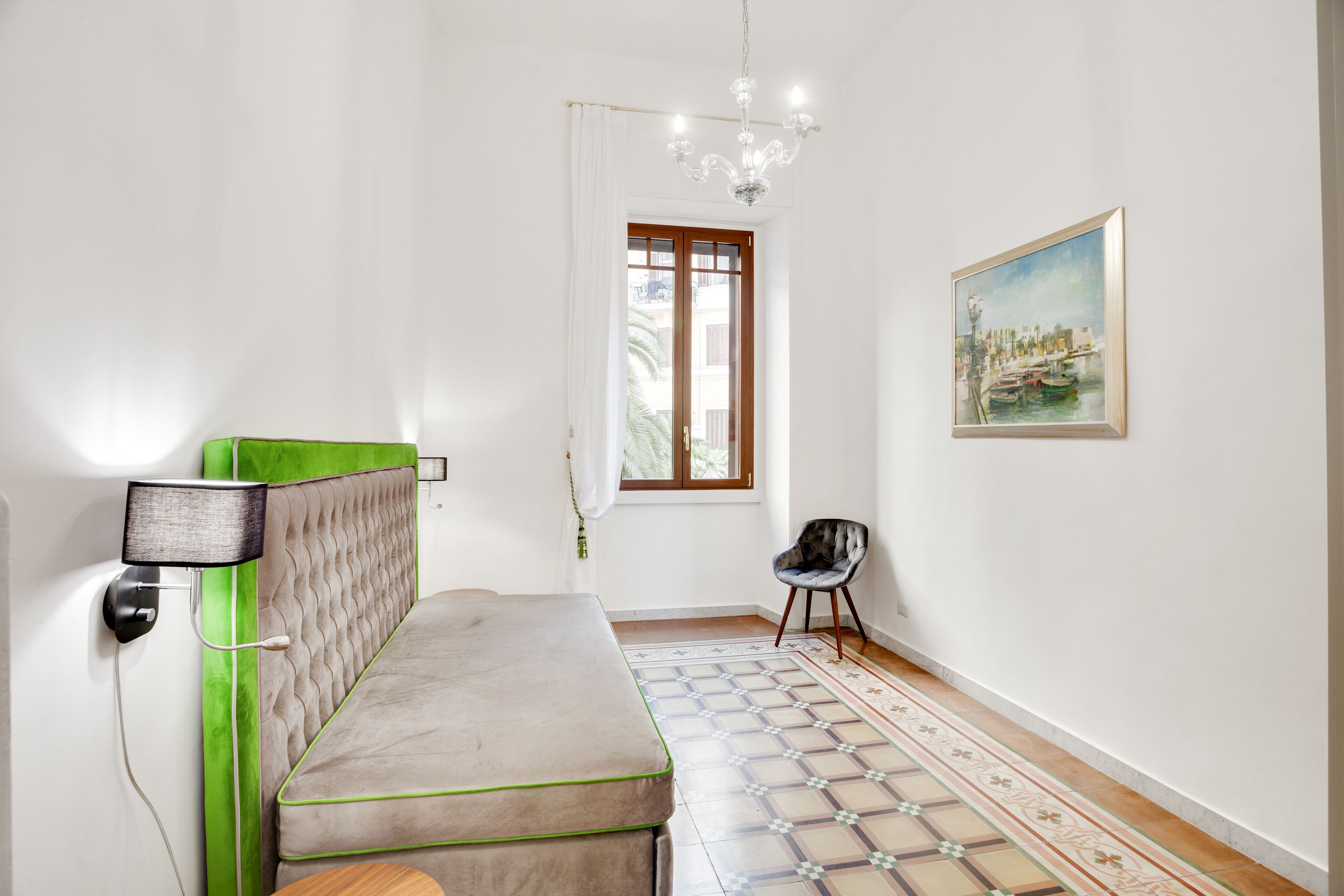 A modern bedroom with a bed, a wall-mounted lamp, a chair, a window, and a painting.