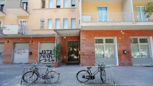 Un edificio de varios pisos con entrada a nivel de calle, un aparcamiento para bicicletas y una puerta de garaje con grafitis.