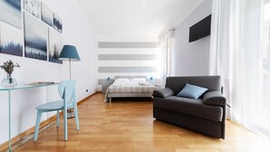 Una habitación moderna con una cama, un sofá, un escritorio con una silla y un televisor montado en la pared.
