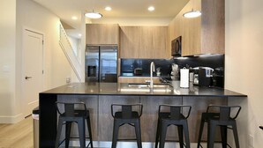 Une cuisine moderne dotée d’un îlot central, d’appareils électroménagers en acier inoxydable et de tabourets de bar.