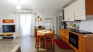 Un espace de vie compact comprenant une table à manger, des chaises, un téléviseur, un coin cuisine et un tapis rouge.