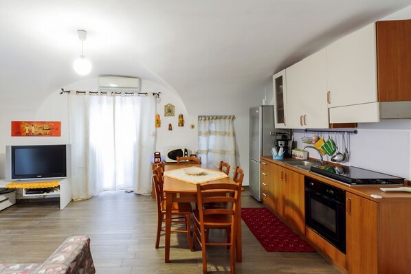 Un espace de vie compact comprenant une table à manger, des chaises, un téléviseur, un coin cuisine et un tapis rouge.