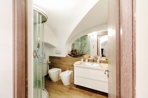 Une salle de bain moderne avec une douche à parois de verre, un bidet, un lavabo avec un miroir et une plante décorative.