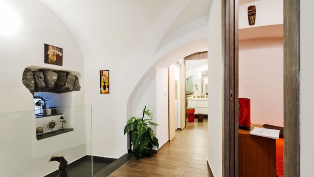 Un couloir doté d’une rambarde en verre, d’une plante en pot, d’un banc en bois et d’une porte donnant sur une autre pièce.