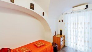 Une pièce avec un mur incurvé, un lit recouvert d’une couverture orange, une commode en bois et une fenêtre ornée de rideaux légers.