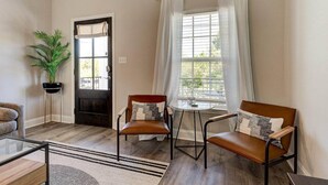 A living room with two leather chairs, a glass coffee table, a potted plant, a door, and a window with curtains.