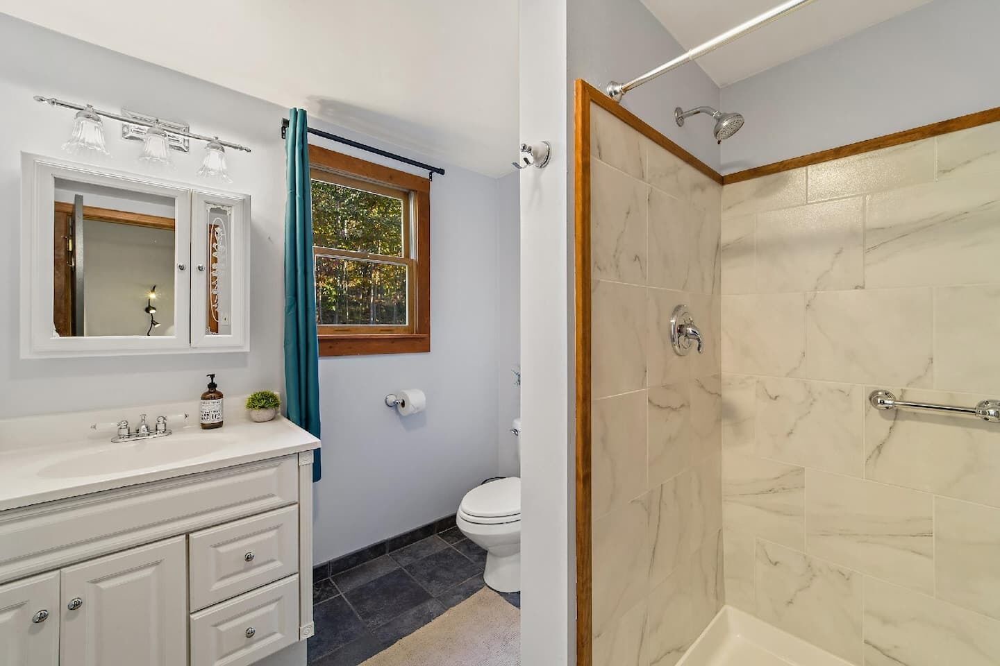 A bathroom with a marble shower, a sink with a mirror, and a toilet.