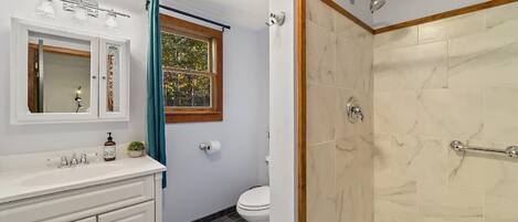 A bathroom with a marble shower, a sink with a mirror, and a toilet.