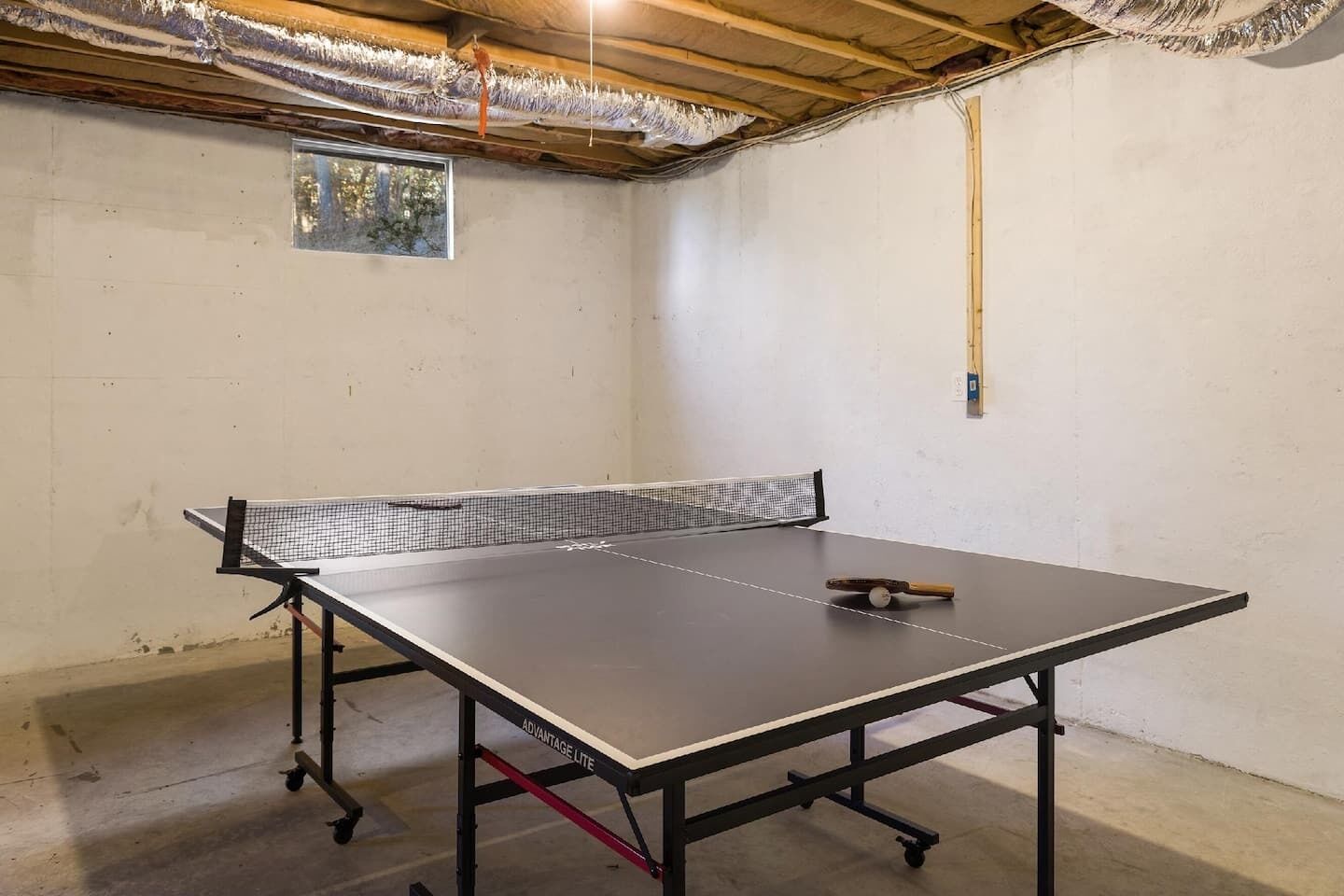 Un tavolo da ping pong in una stanza con pavimento in cemento e soffitto in legno.