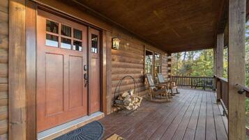 Una baita di legno con veranda, una porta d'ingresso e un piccolo spazio esterno arredato con sedie e un tavolo.