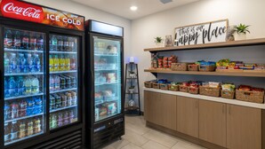 A vending area with Coca-Cola and Sprite refrigerated drinks, a 'happy place' sign, and snack baskets on shelves.