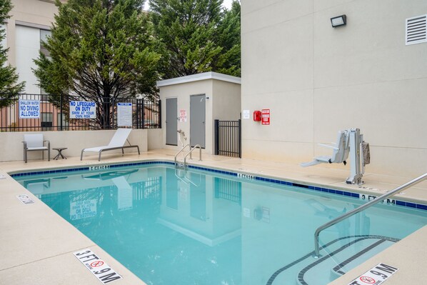 A swimming pool with safety signs, a lifeguard station, and lounge chairs.