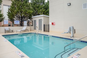 Una piscina con señalización de seguridad, una estación de salvavidas y sillas de descanso.