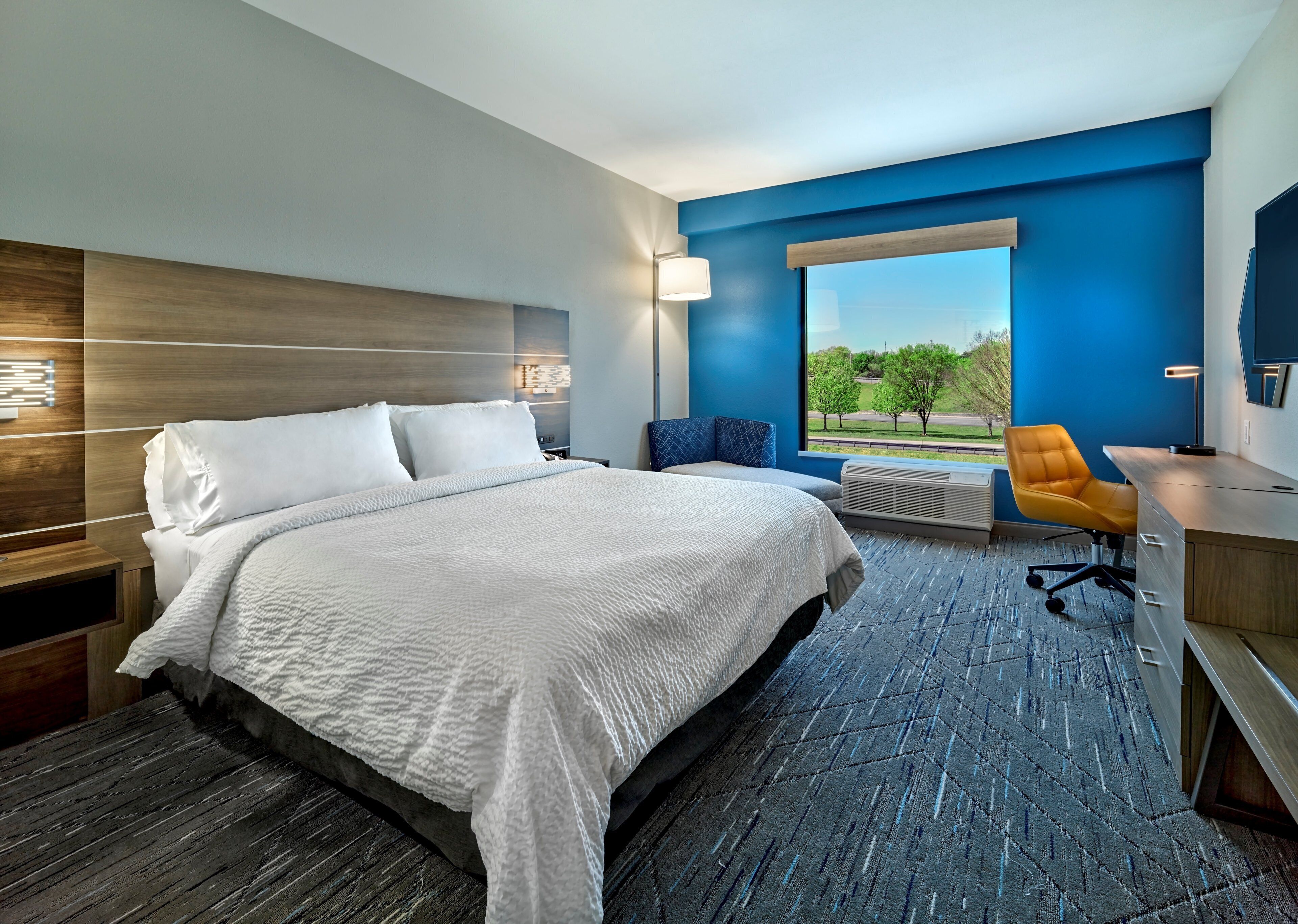 A hotel room with a large bed, a desk, a chair, and a view of the outdoors.