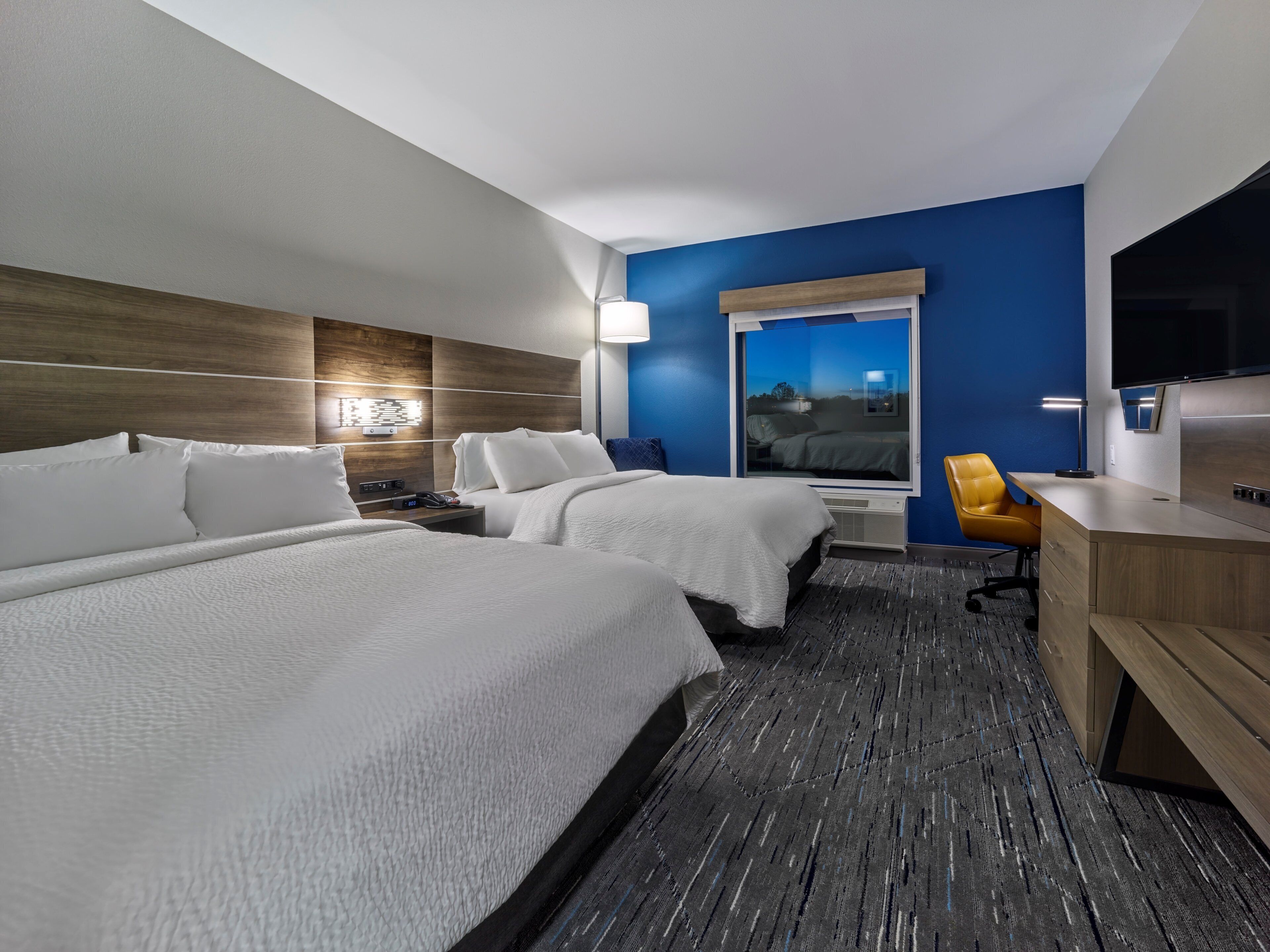 A hotel room with two beds, a desk, a chair, a TV, and a window with a view.
