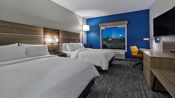 A hotel room with two beds, a desk, a chair, a TV, and a window with a view.