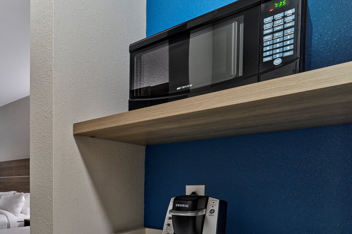 Una kitchenette equipada con microondas, cafetera y soporte para cápsulas de café.