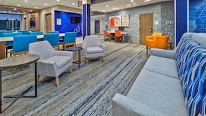 A modern hotel lobby with seating areas, a reception desk, and a large screen displaying the hotel's name.