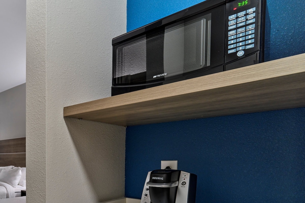A kitchenette with a microwave, a coffee maker, and a coffee pod holder.