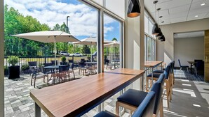 A modern indoor seating area with a wooden table and blue cushioned chairs, large windows offering a view of the outdoors, and pendant lighting. - Holiday Inn Express Huntsville Space Center by IHG (Huntsville)