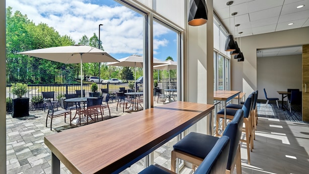 A modern indoor seating area with a wooden table and blue cushioned chairs, large windows offering a view of the outdoors, and pendant lighting.