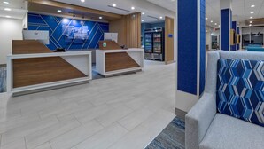 A modern reception area with two reception desks, a seating area with patterned cushions, and a refrigerator with beverages.