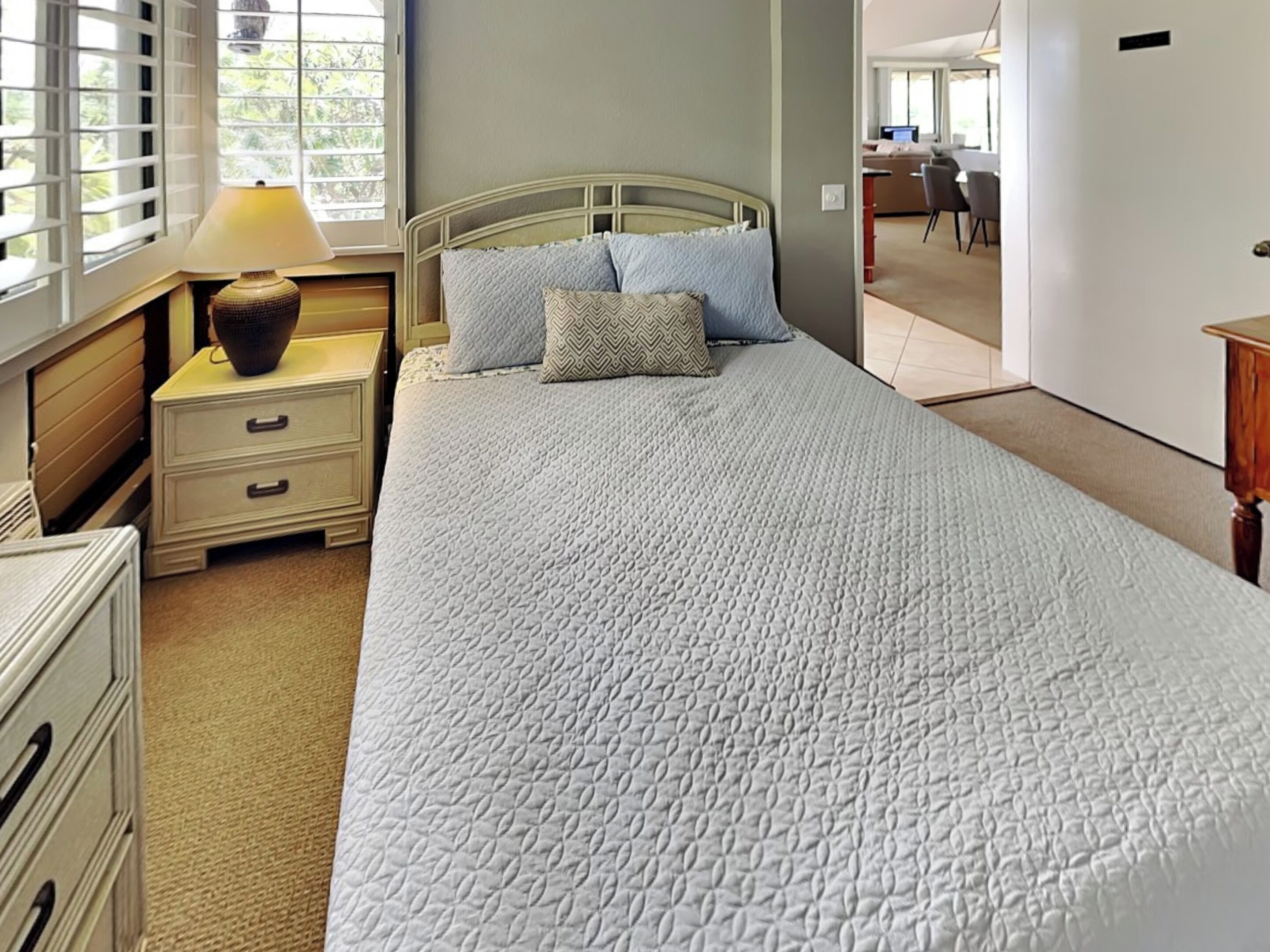 A neatly made bed with a quilted cover, a bedside lamp, and a nightstand with drawers.