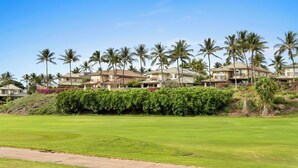 Un parcours de golf doté d’un terrain verdoyant bien entretenu, bordé de palmiers et entouré de bâtiments résidentiels, avec des collines en arrière-plan.