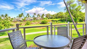 Un balcon avec une table et des chaises donnant sur un terrain de golf, bordé de palmiers, et sous un ciel dégagé.