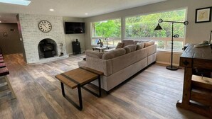 Un salon moderne avec une cheminée, un canapé, une table basse et une grande fenêtre donnant sur un paysage verdoyant.