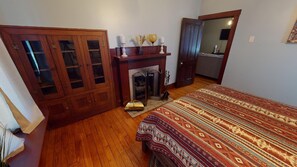 A bedroom with a wooden wardrobe, a fireplace, a bed with a patterned bedspread, and a mirror on the wall. - Vacation Cottage near Wayne National Forest ATV Trail Head, Hot Tub & more! (Nelsonville)