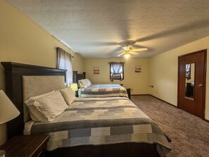 A hotel room with two beds, a ceiling fan, a door, and a carpeted floor.