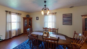 Uma sala de jantar com mesa de madeira, cadeiras, um candelabro e um tapete azul.