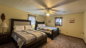 A bedroom with two beds, a ceiling fan, a nightstand with a lamp, and a wall-mounted air conditioner.