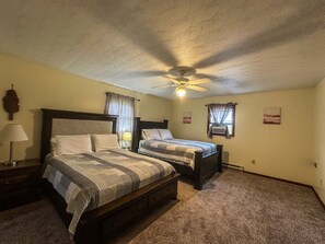 Une chambre avec deux lits, un ventilateur de plafond, une table de chevet avec une lampe et un climatiseur fixé au mur.